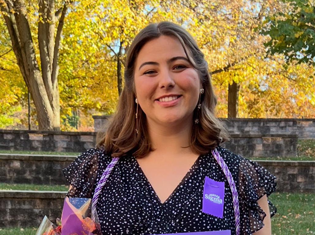 Graduating senior Lara Hummer stands smiling with fall foliage