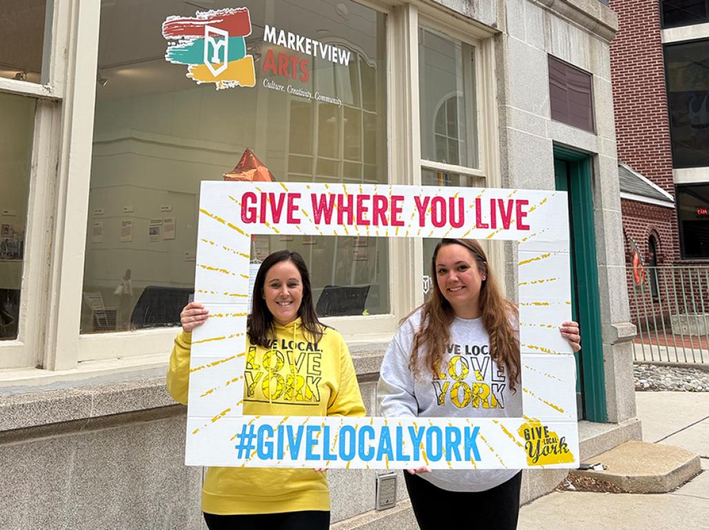 Two women pose with a Give Local York sign in front of Marketview Arts