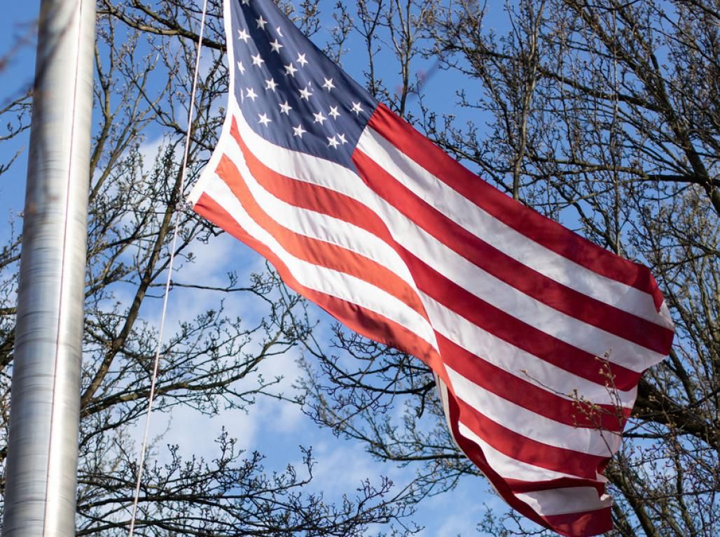 American flag on a flag pole with trees and sky behind it.
