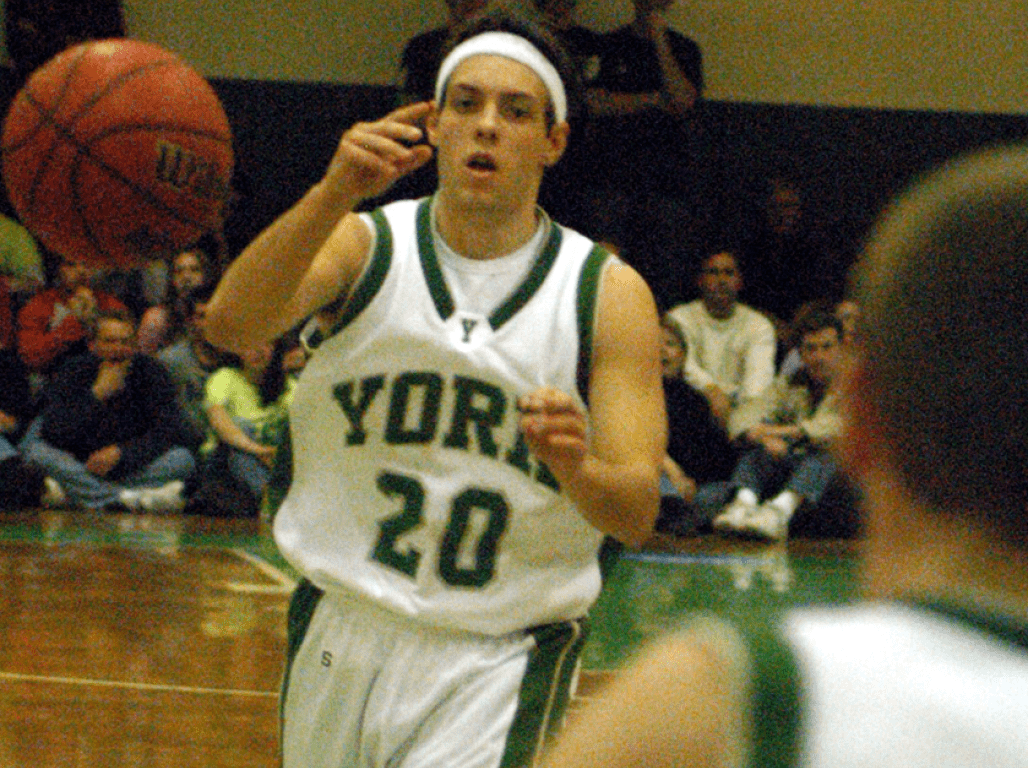 Two individuals engaged in a game of basketball, the person passing the ball is wearing a "York 20" athletic jersey.