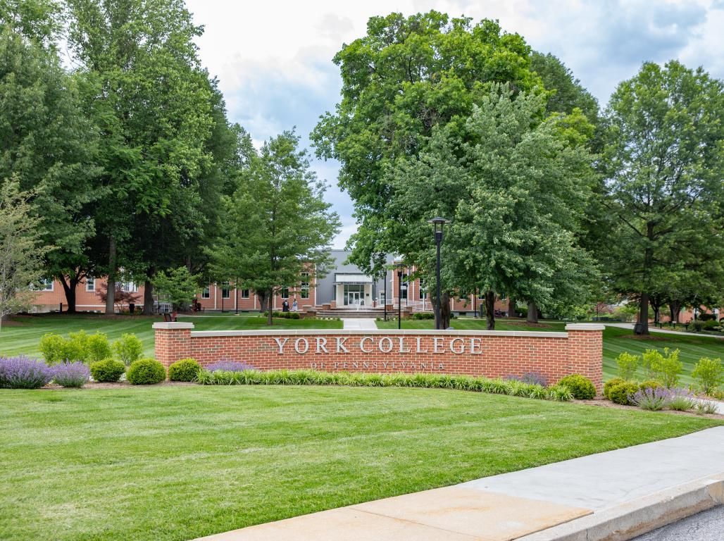 Summer photo of the York College campus with the sign, fountain and library in the background