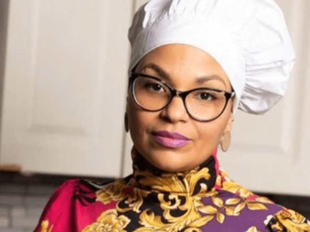 Person in a chef's hat standing in a kitchen with a resolute expression.