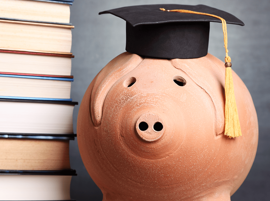 Piggy bank wearing a graduation cap sitting next to a stack of books.