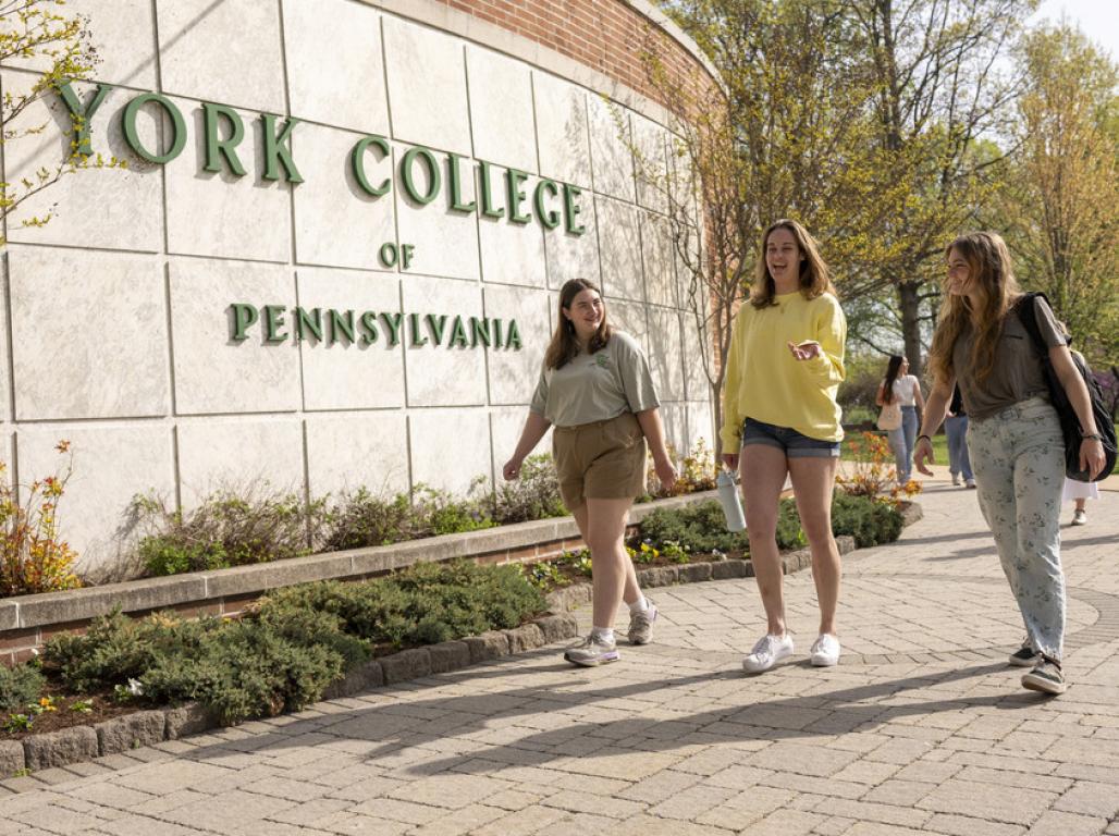 The York College sign on main campus with three students walking in front of it
