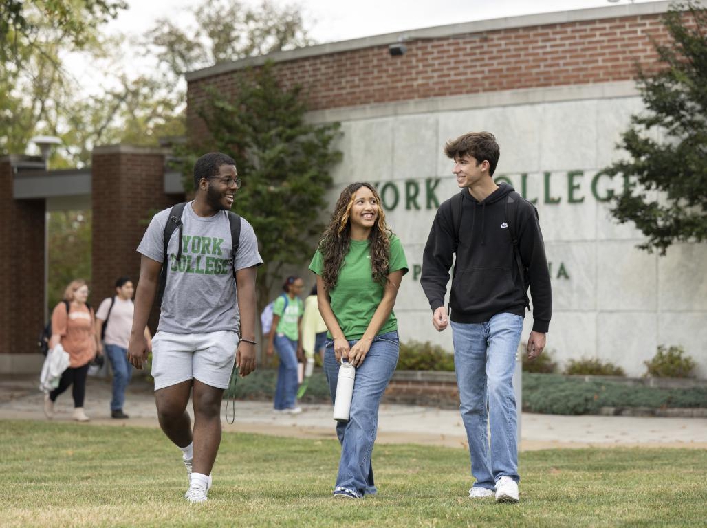 Three students walking together in front of a York College sign