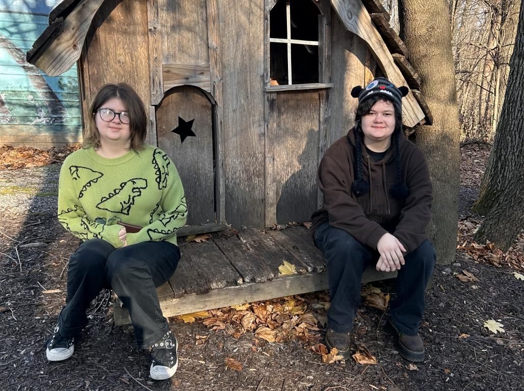 Siblings Aeris and Isis Brewer sit side by side outdoors on a fall day.