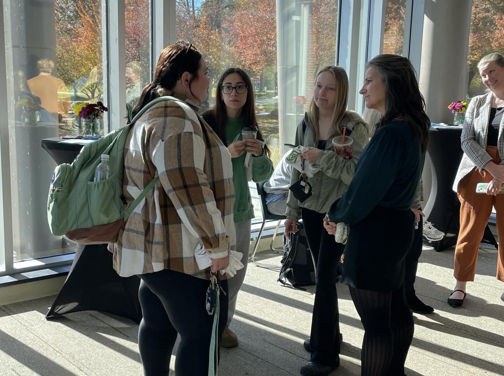 A group of people standing in a bright room, engaged in conversation.