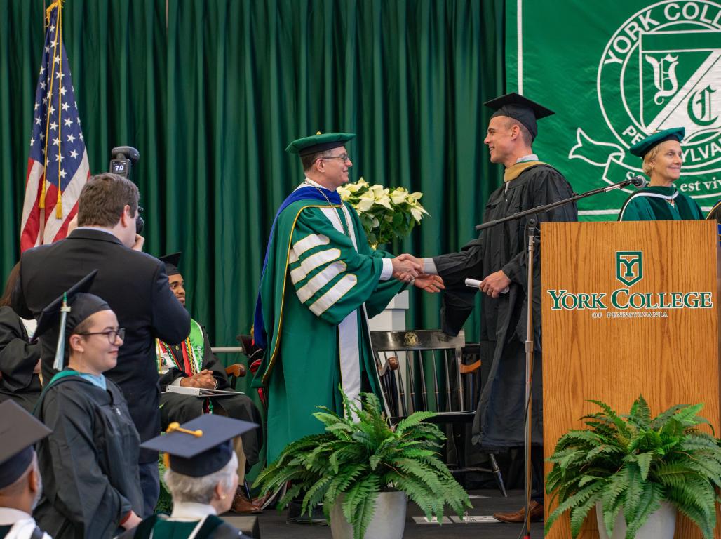 Dr. Burns shakes hands with a graduate during a commencement ceremony.