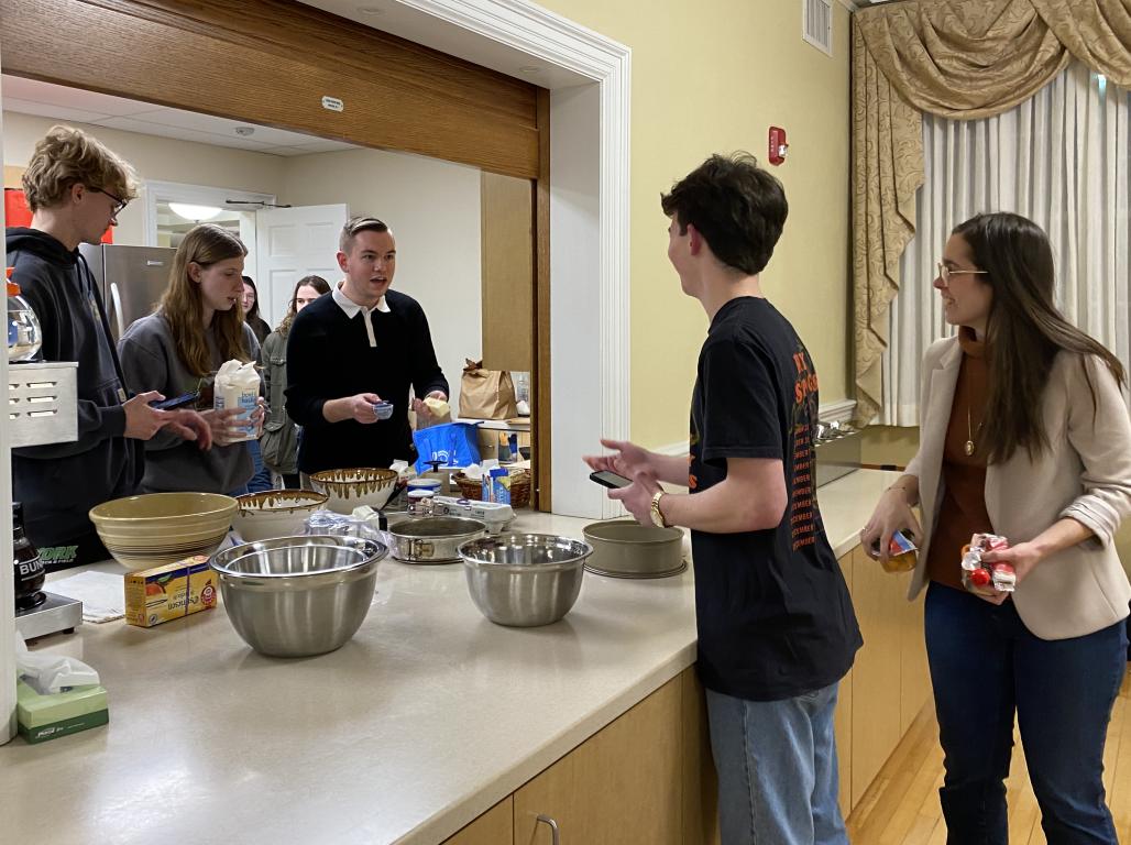 Students stand on either side of an open window with bowls and food