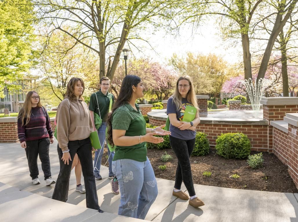 A group of people walking and talking together on a beautiful spring day. A fountain is visible in the background.