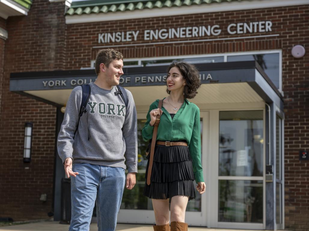 Two York College engineering majors walk and talk in front of the Kinsley Engineering Center building entrance.