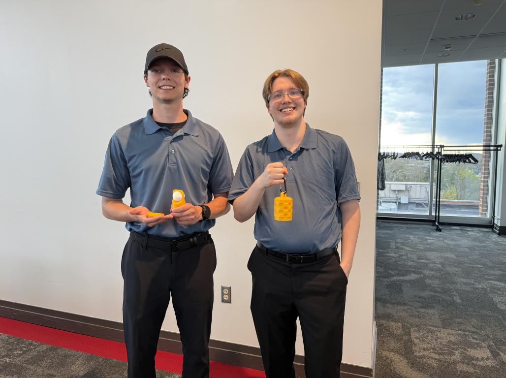 Two people wearing grey polo shirts and black pants holding compact golf ball cleaning devices.