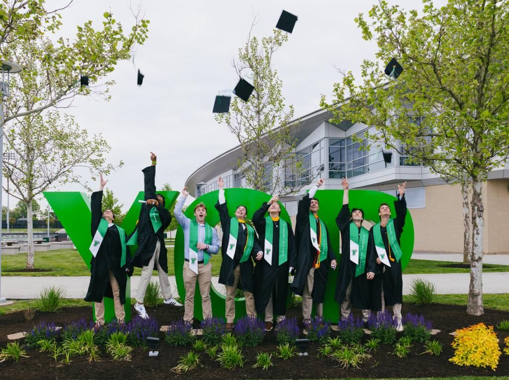A group of college graduates toss their caps in front of green YCP letters.
