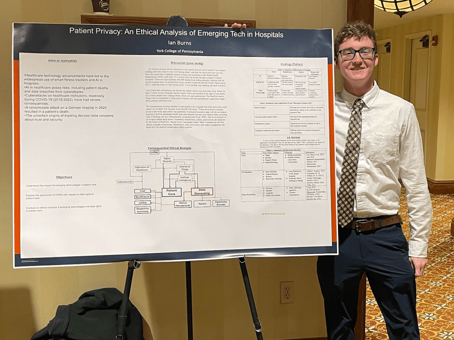 Student in professional attire smiles while showcasing a research poster titled "Patient Privacy: An Ethical Analysis fo Emerging Tech in Hospitals."