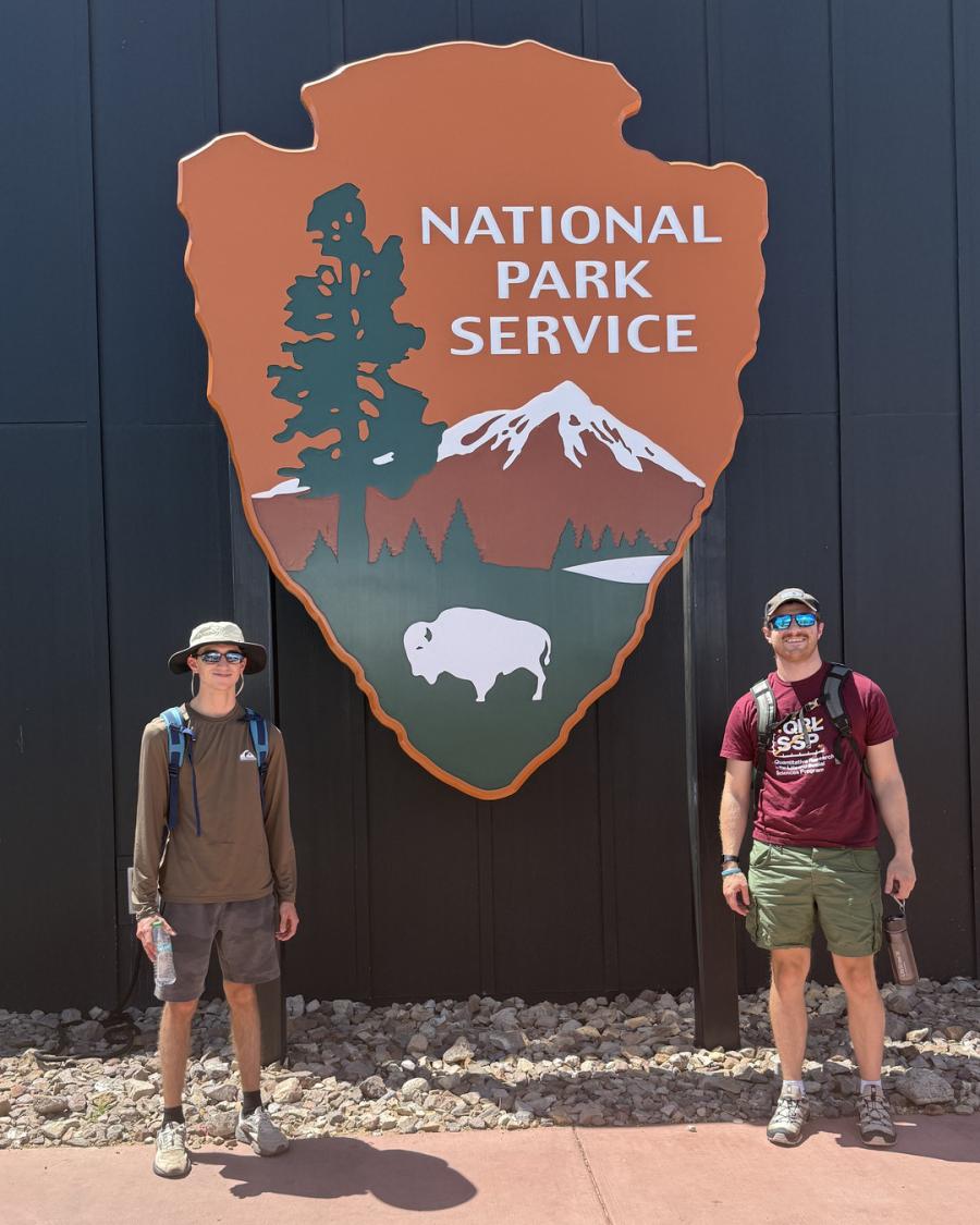 van Gibbs and Alex Glatfelter stand beside a large National Park Service sign