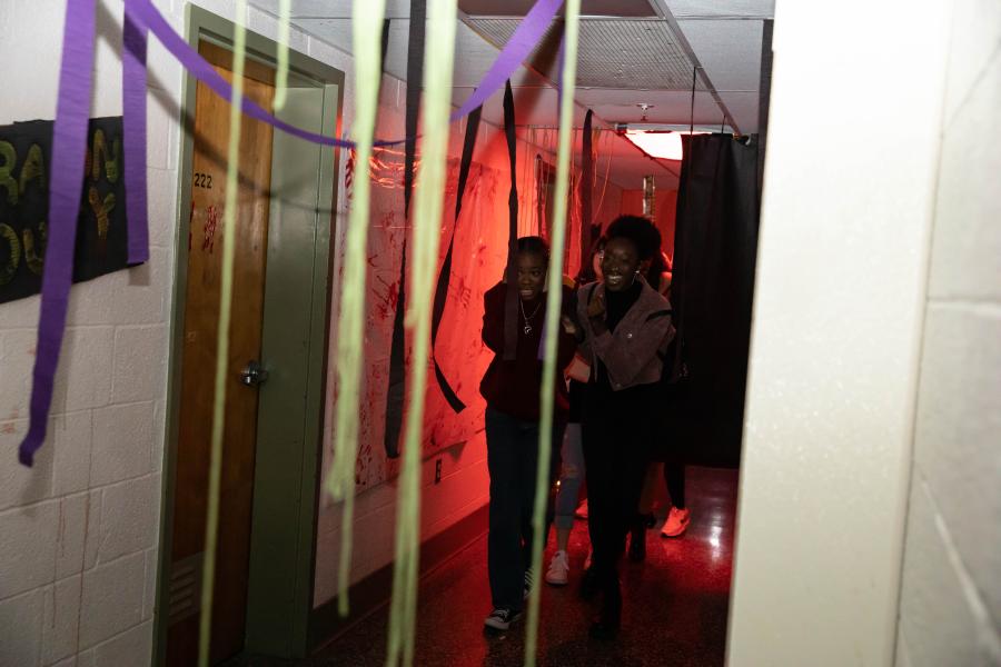 People walking through a haunted house hallway with streamers in the foreground,