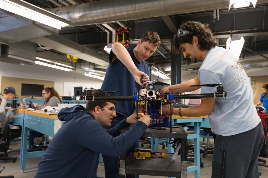 Three individuals working together on a drone in an engineering lab.