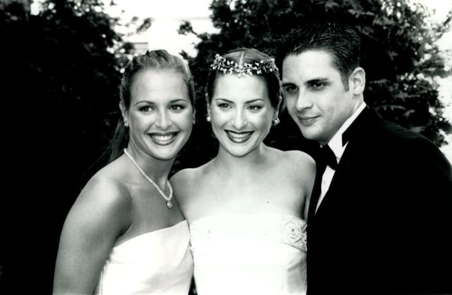 A black-and-white photo shows a man in a tuxedo posing outdoors with two women in formal dresses.