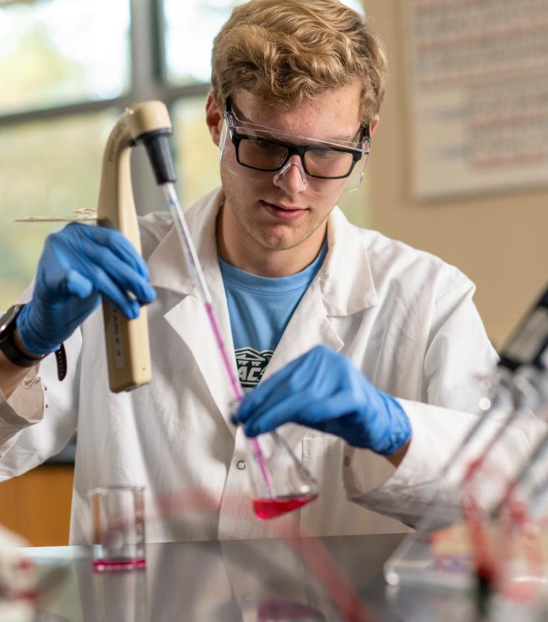 A biology student in the lab inputting a liquid into a beaker.