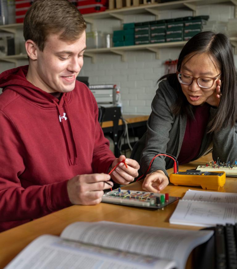 Two students use a electrical testing device on a circuit board.