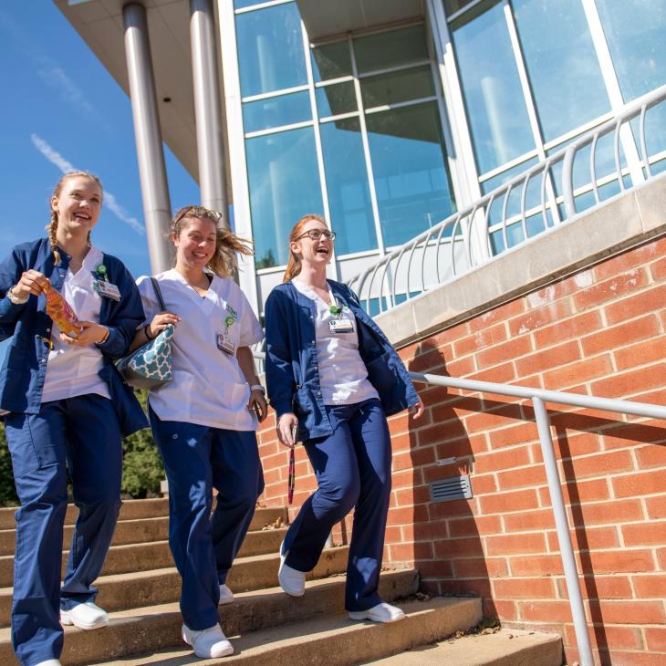 Three nursing students walk down outdoor stairset on a sunny day