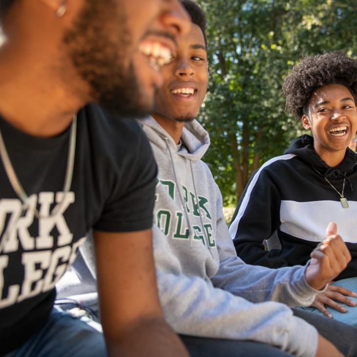 Three students smile while sitting outdoors on campus