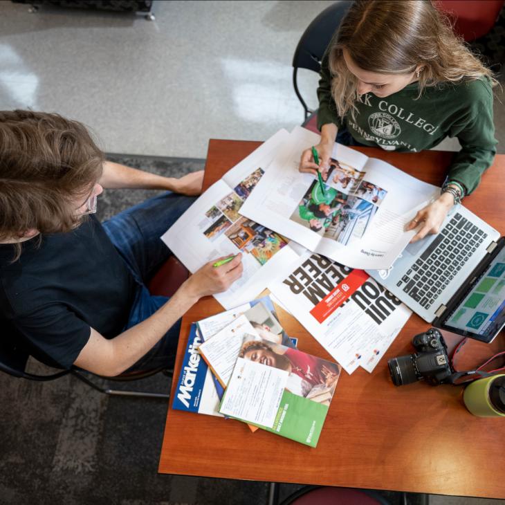 Two Students go through class materials while discussing them.