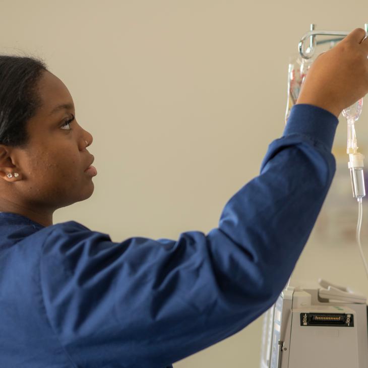 A nursing student hangs a bag of fluid on a stand.