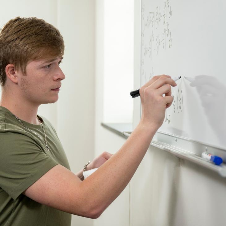 A Student writes out a math problem on a whiteboard