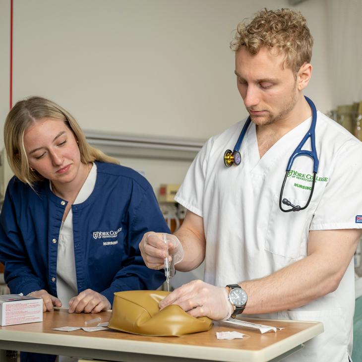 Two students learning how to give a shot.