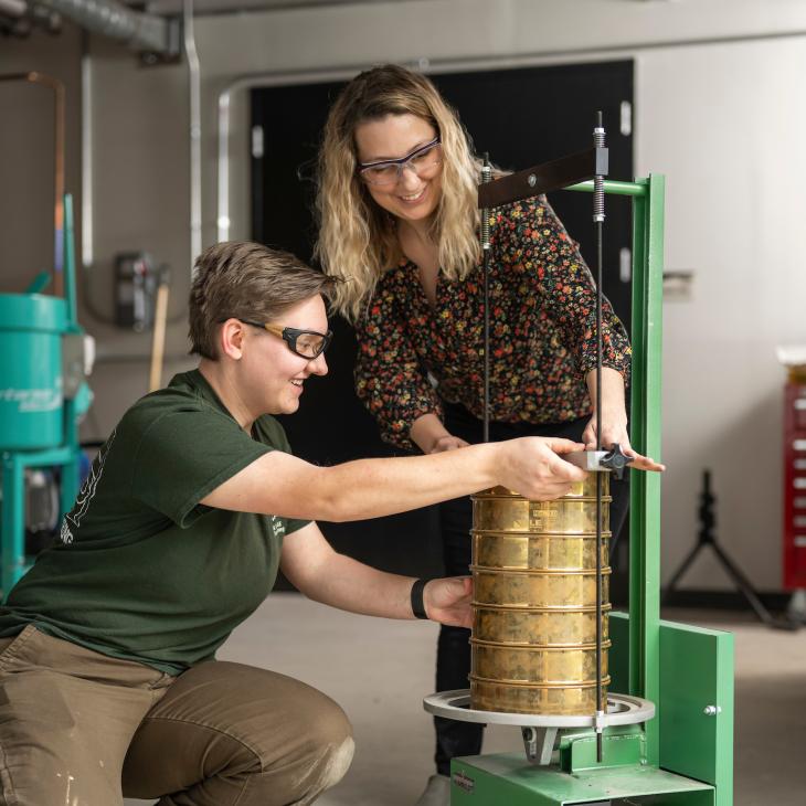 Two students measure the height of a stack of test sieves using a machine.