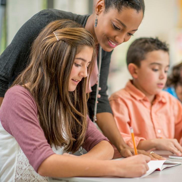 A teacher teaching a group of students as they are completing a worksheet.