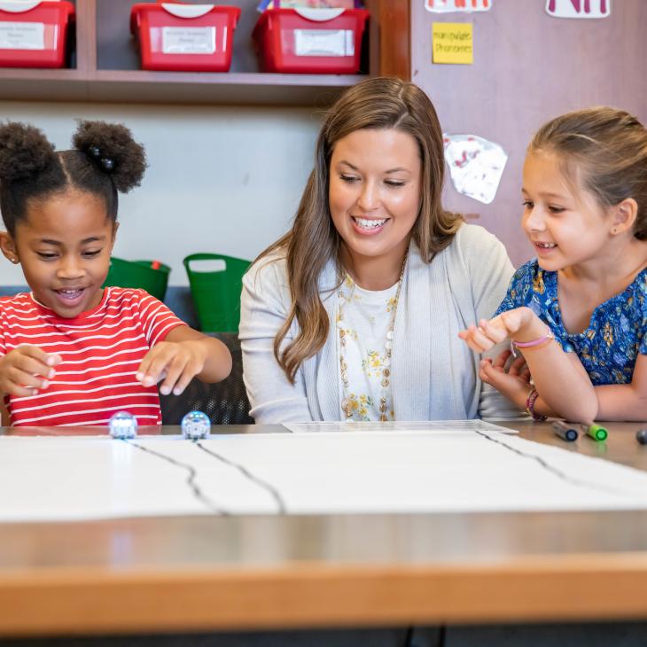 2 young students are working on a project while a teacher overlooks