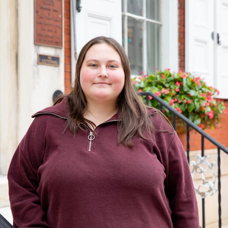 Kristie Houck stands in front of the front stoop of the Center for Community Engagement. Flower boxes and the brick face of the building are visible in the background.