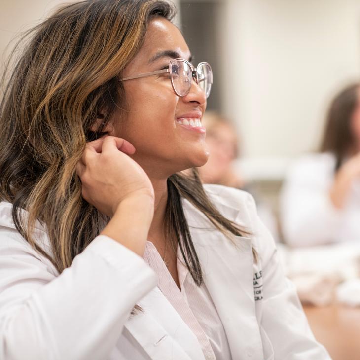 Graduate Nursing student in white doctors coat smiling in a classroom