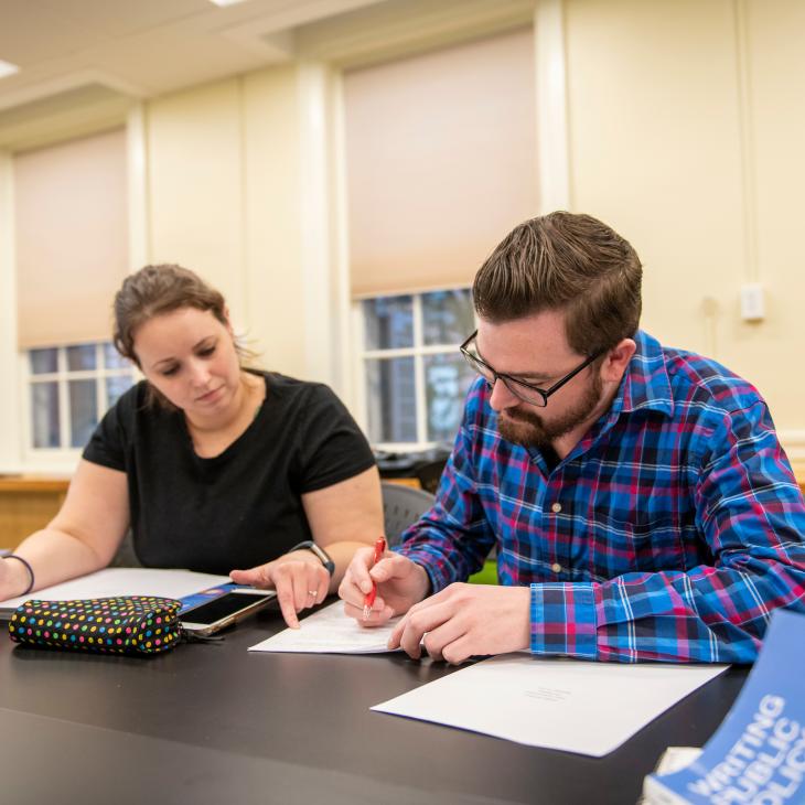 Two MPPA students studying in a classroom. Student on the lest is wearing a black shit, and the student on the right is wearing a primarily blue flannel