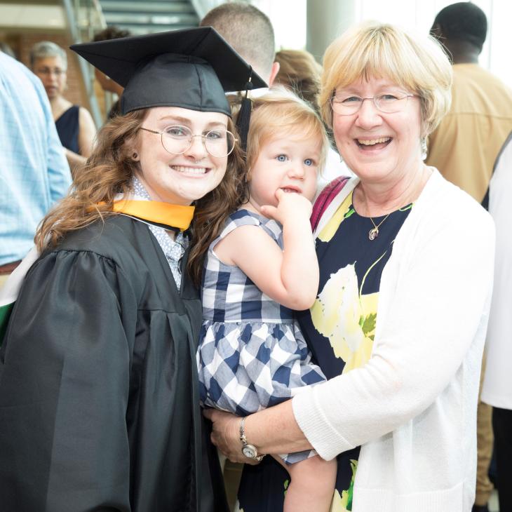 A student in cap and gown poses at a graduation ceremony with family members.