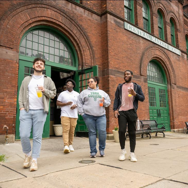 Four students walking downtown in front of the Central Market House.