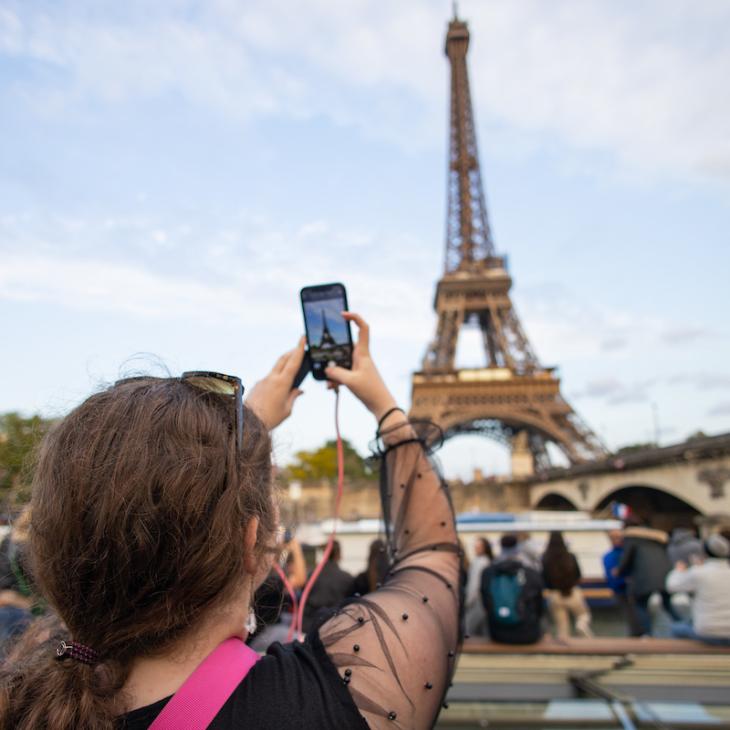 A student holds up a cell phone to take a photo of the Eiffel Tower.