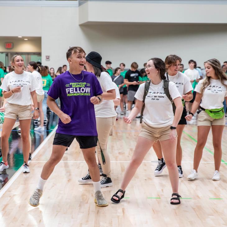 A group of new students dance in the gymnasium with their peer advisor.
