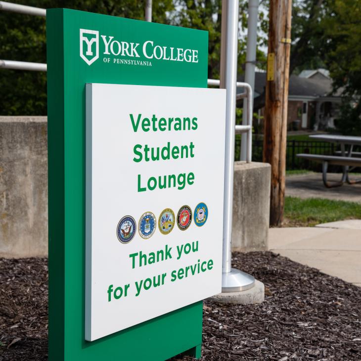 A sign in front of a campus building reads "Veterans Student Lounge. Thank you for your service."