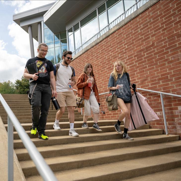 Four students chat and smile as they walk down a set of outdoor steps on campus.