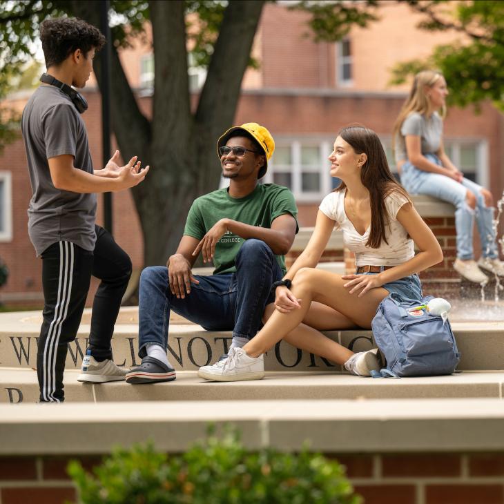 Three students gather by a fountain at the center of campus, laughing as they chat.