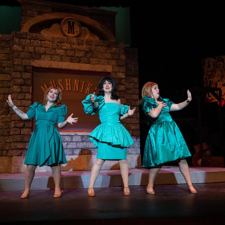 Three students dressed in '50s-style costumes sing on stage during a performance of Little Shop of Horrors.