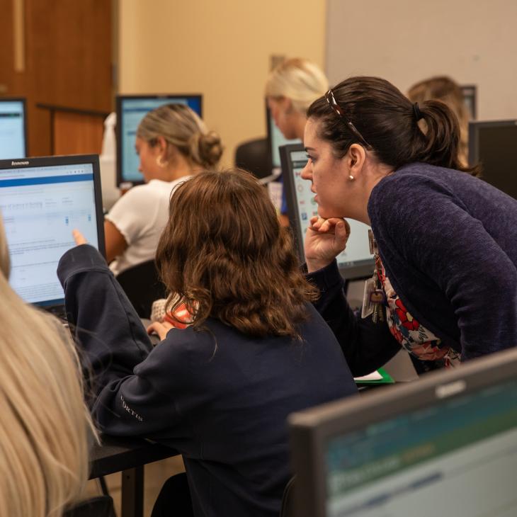 An advisor looks over a student's shoulder as they register for classes in the computer lab.