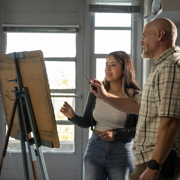 Student and professor drawing on an easel in a classroom