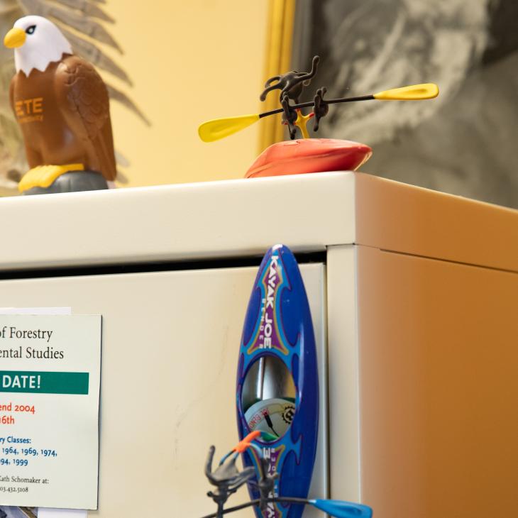 A small toy magnetic kayak with bright blue oars is attached to the top drawer of a filing cabinet.