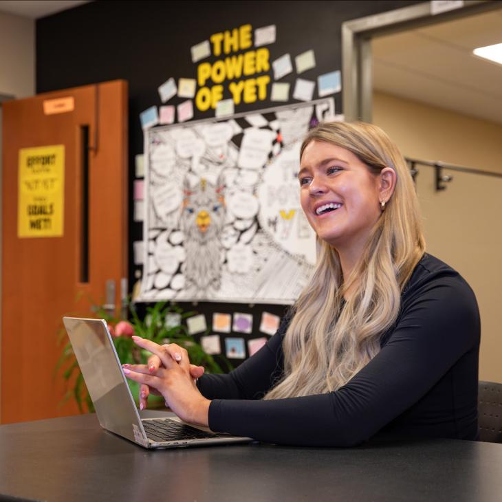 Tutor Marianna Lally smiles in the Writing Center as she works on a laptop.