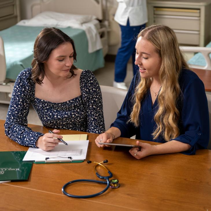 Two healthcare students talking in a nursing lab.