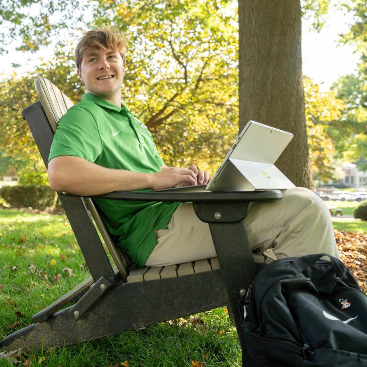 Student in green polo sitting outside in a chair looking at an iPad
